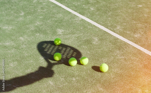 The shadow of a racket with a yellow ball on the green carpet of the tennis court.