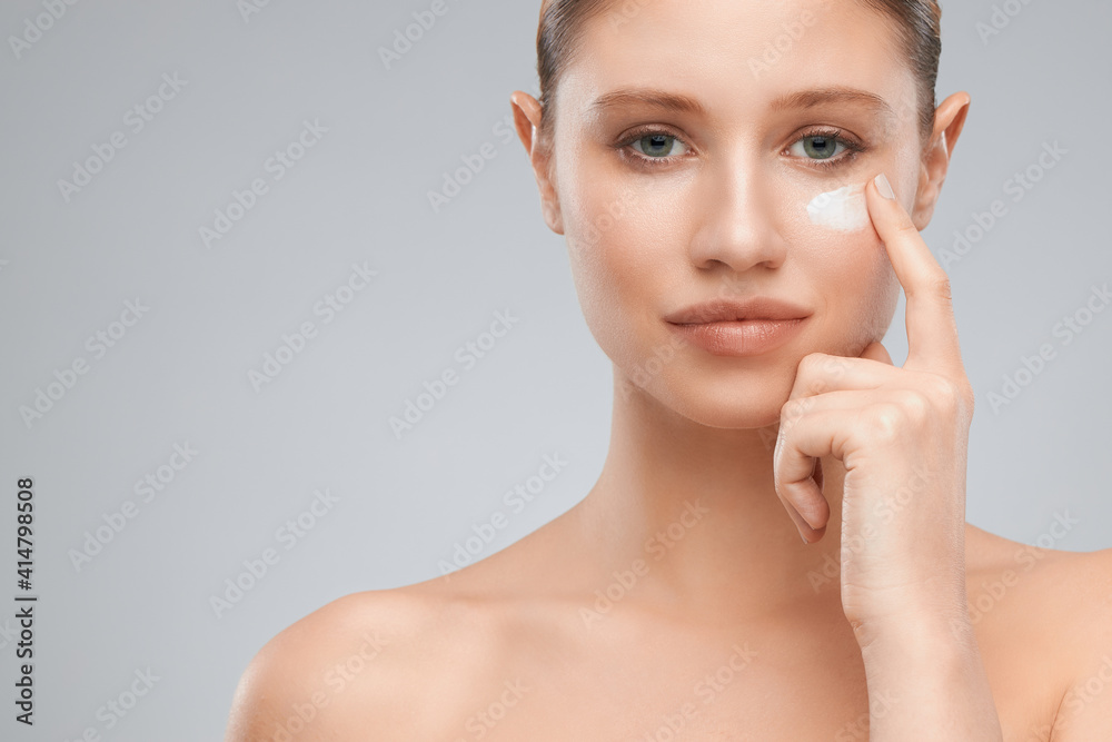 Beautiful blond woman putting moisturizer on her face while standing in studio. Beautiful blond woman putting moisturizer on her face while standing in studio.