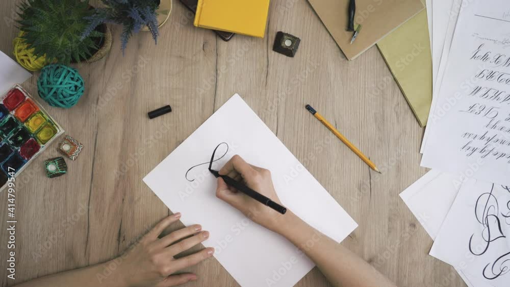 Female Hand is Writing Calligraphic Twirl view from above Female Hand is Writing Calligraphic Twirl view from above