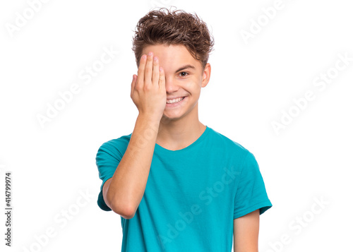 Handsome teen boy looks with one eye while covering his other eye with his hand, isolated on white background