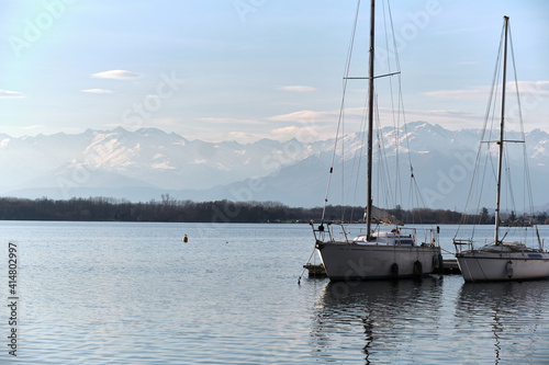 two sailboats moored on the pier of an alpine lake with the mountains in the background © Ivan