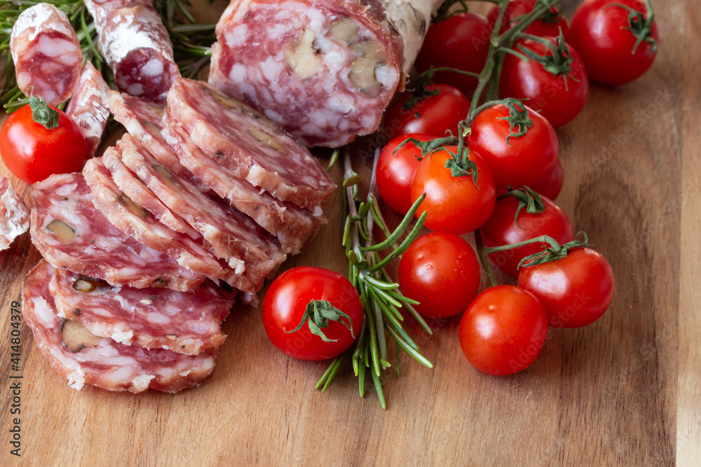 Sliced Air-dried salami with rosemary and cherry tomatoes - wood background Sliced Air-dried salami with rosemary and cherry tomatoes - wood background
