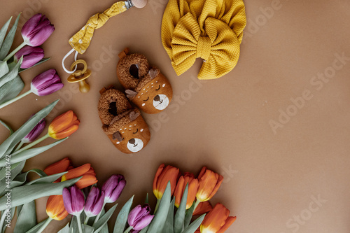 Set of baby shoes, toys, accessories, fresh spring tulips on brown background. Newborn stuff. Flat lay, top view