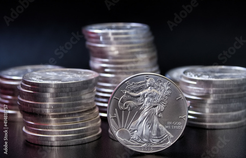 A silver Eagle coin in front of stacks of silver eagle coins