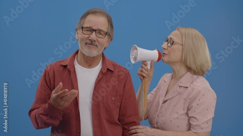 The old woman shouts with a megaphone to her husband, who never listened to him and did not value his thoughts. The husband still does not listen to his wife.Blue background.