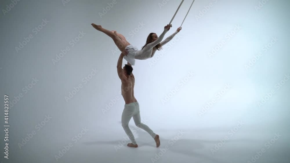 Aerial straps duo wearing white costume on white background doing performance in slow motion. Concept of romantic relation ship in couple Aerial straps duo wearing white costume on white background doing performance in slow motion. Concept of romantic relation ship in couple