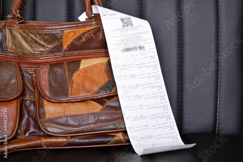 Women leather bag from which hangs long store receipt for purchase on black leather background