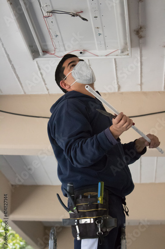 A Latin janitor repairing light on a school passageway