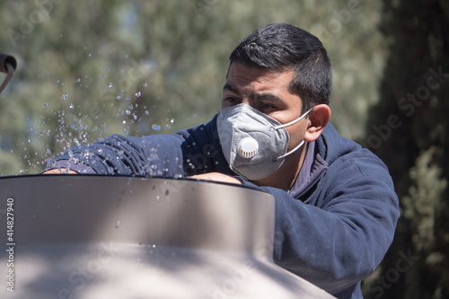 Hombre mexicano de mediana edad revisa su suministro de agua después de desabasto durante la pandemia COVID-19 porta mascarilla KN95 photo