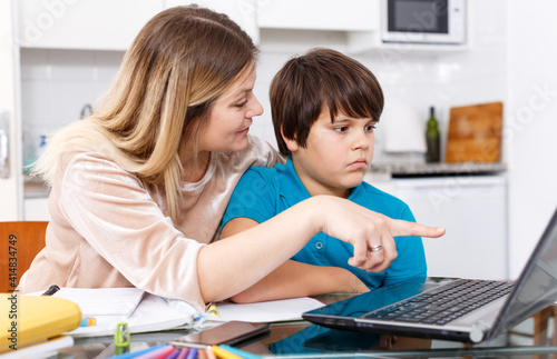 Portrait of emotional woman and boy doing homework with laptop at kitchen