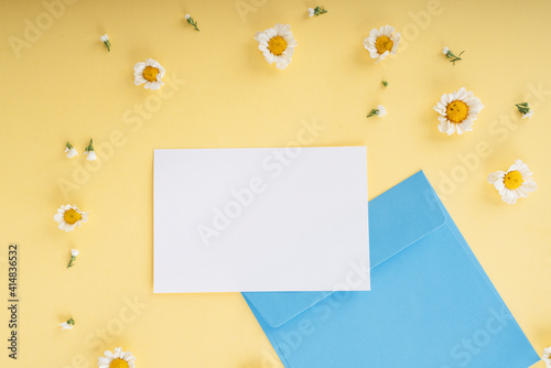 Mock up white paper with blue enclosed letter over yellow backgroud and white flower.