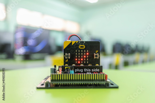 Microbit Educational microcontroller board showing a checkmark. With a backdrop of a computer room in the concept