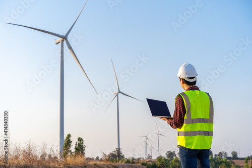 male engineer working with laptop computer against wind turbine farm