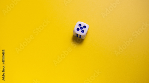 White dice with round dots number five on yellow background close-up. Concept of gambling and chance
