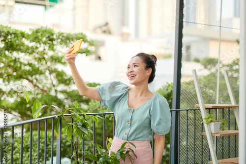 Cheerful young Asian girl having a video call with her phone when standing o balcony.