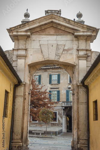 View on Piazza Martiri di Belfiore, Brescia, Italy. Ancient arch between the Broletto palace and the Martiri di Belfiore square. House with gray facade, balcony and windows with green wooden shutters photo