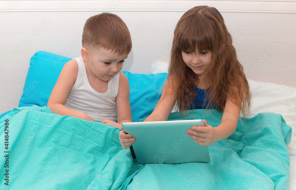 Young children enjoy digital gadget in bedroom of house. Children lie on bed and play on tablet. Education technology of learning concept of leisure. A child with gadget Young children enjoy digital gadget in bedroom of house. Children lie on bed and play on tablet. Education technology of learning concept of leisure. A child with gadget