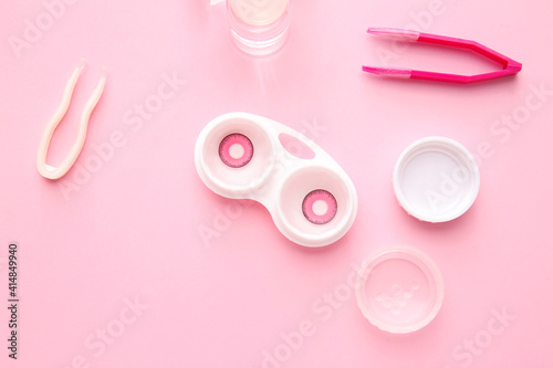 Bottle of solution, tweezers and container with contact lenses on color background