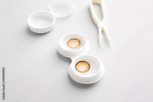 Container with contact lenses and tweezers on light background