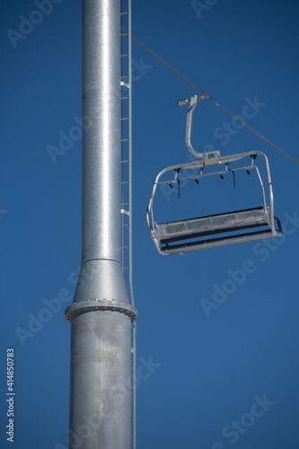 empty ski lift chair silver metal metallic seat next to ski lift pole or tower against blue skies at ski resort vertical format clean space for type photo
