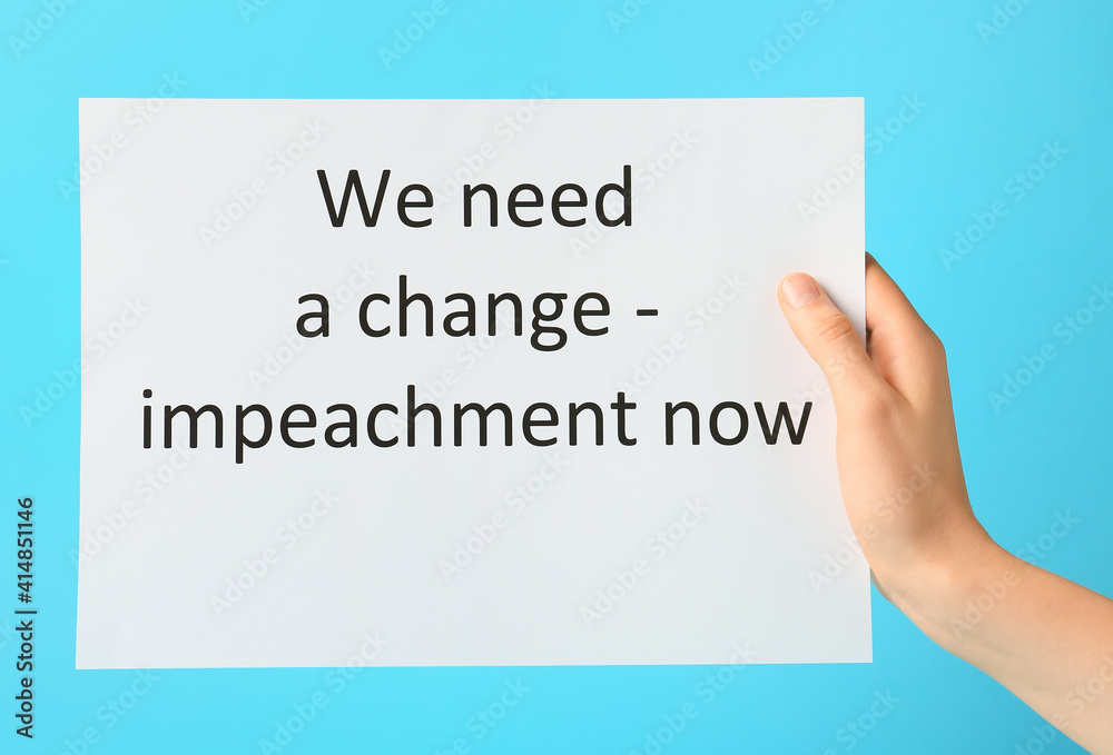 Hand holding paper with text WE NEED A CHANGE - IMPEACHMENT NOW on color background Hand holding paper with text WE NEED A CHANGE - IMPEACHMENT NOW on color background