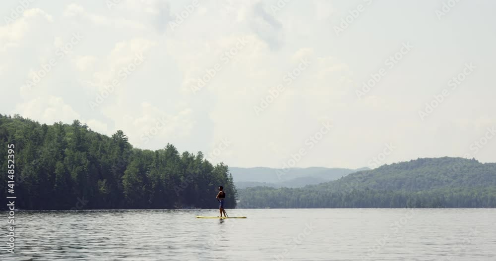 Paddle boarder out on a leisurely ride on overcast summer day - wide shot Paddle boarder out on a leisurely ride on overcast summer day - wide shot