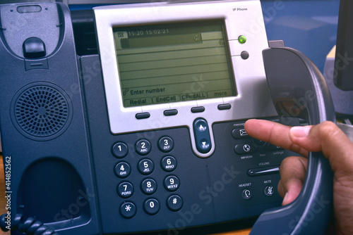 Hand of man holding telephone handset and pressing button on keypad, office desk