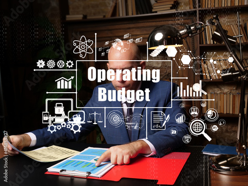 Financial concept about Operating Budget with inscription. Young finance market analyst in eyeglasses working while sitting at wooden table on background.