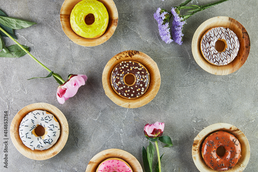 Multicolored donuts with glaze and splashes with flowers on a gray background Multicolored donuts with glaze and splashes with flowers on a gray background
