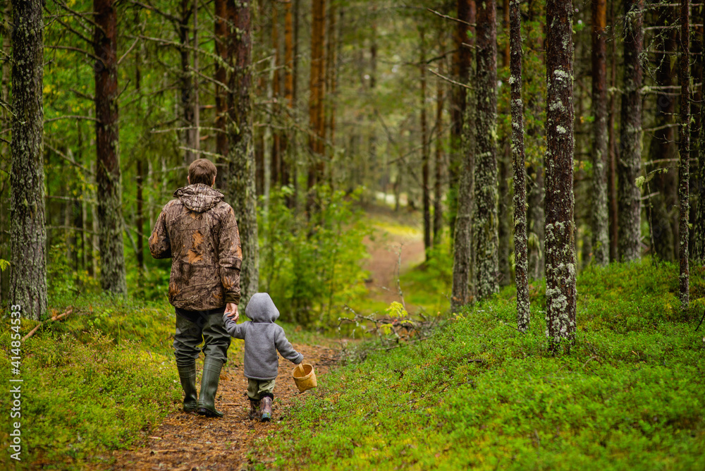 a small boy and an adult walk through the woods to a wooden house, selective focus