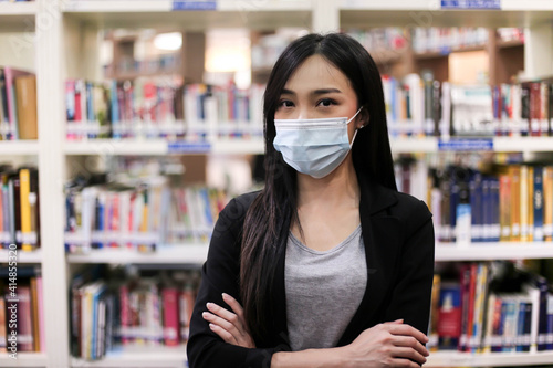 Beautiful Asian librarian woman wear face masks to prevent coronavirus, or COVID-19 new normal lifestyle in the library.