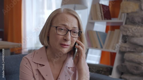 Blonde old lady who speaks very sad on her cell phone at home is unhappy. Concept of talking over the phone.