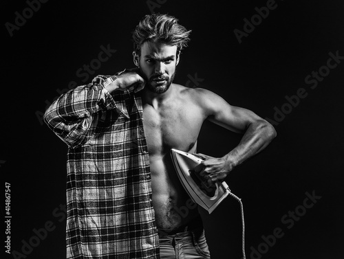 Sexy young shirtless man with messy hair, irons plaid shirt on black background. © Volodymyr