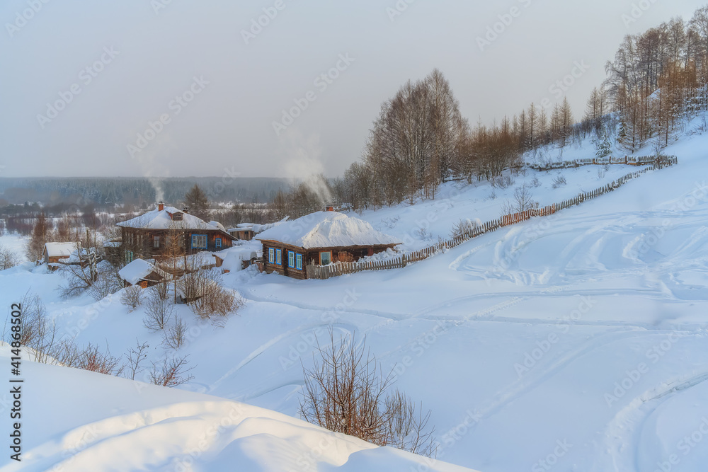 Fototapeta premium A panoramic view of the winter provincial Cherdyn (Northern Urals, Russia) - a city on several hills where people go skiing. wooden houses with smoke coming out of pipes, pure snow