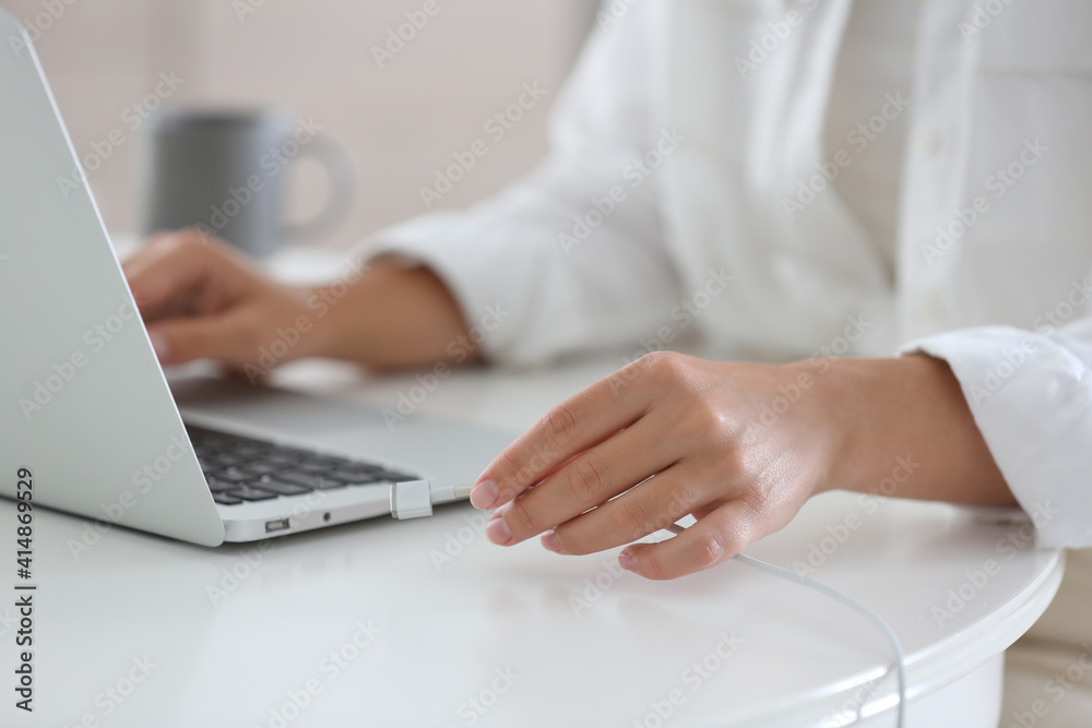 Woman connecting charger cable to laptop at white table, closeup Woman connecting charger cable to laptop at white table, closeup