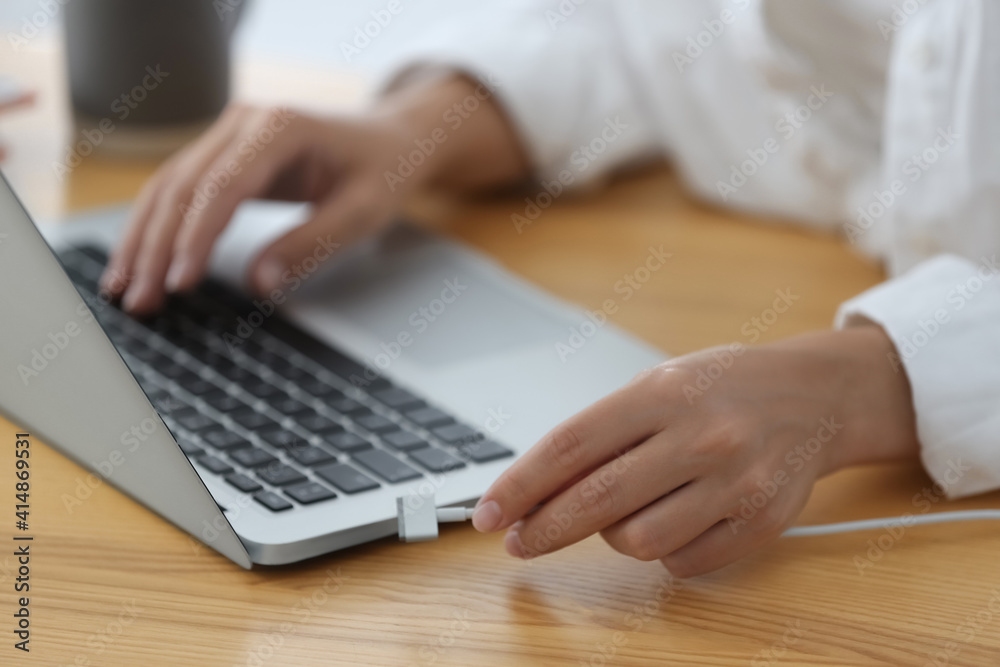 Woman connecting charger cable to laptop at wooden table, closeup Woman connecting charger cable to laptop at wooden table, closeup