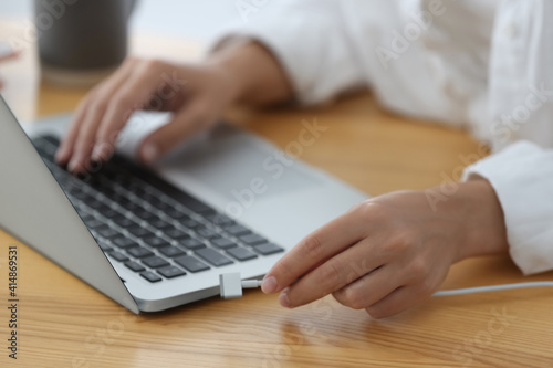 Woman connecting charger cable to laptop at wooden table, closeup