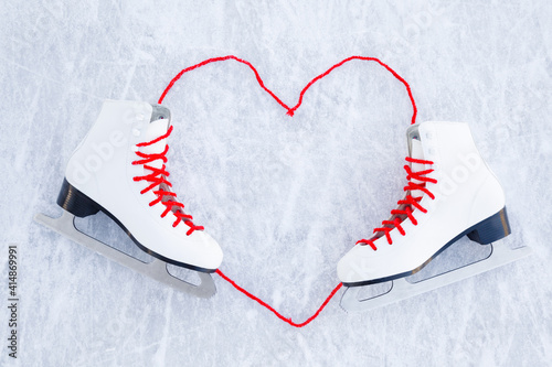 Heart shape created from bright red shoelaces. White female figure skates on ice background. Closeup. Empty place for motivational, inspirational text, quote or sayings. Top down view. photo