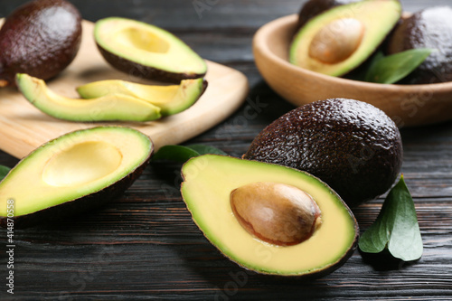 Whole and cut avocados with green leaves on dark wooden table, closeup