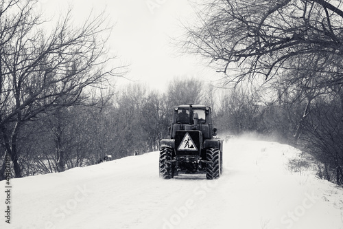 Black and white old tractor clears the snow-covered road from snow blockages