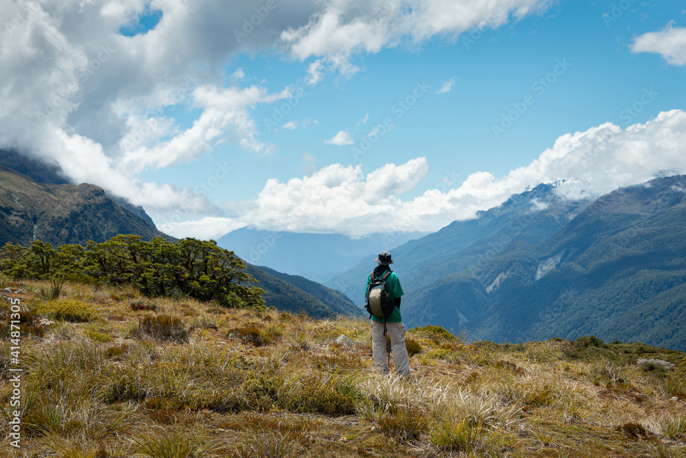 A tramper standing on top of Key Summit and enjoying the views of rolling mountains at Routeburn Track, South Island, New Zealand