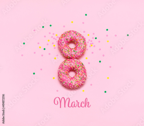 A greeting card for women's day with donuts in the form of the number eight, covered with pink icing, lying on a pink background. Beautiful pink buns, presented for the holiday on March 8.