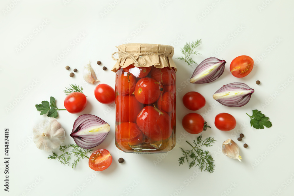 Jar of pickled tomatoes and ingredients on white background
