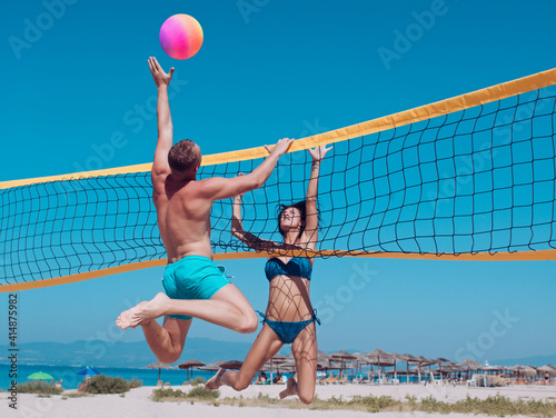 People playing beach volleyball having fun in sporty active lifestyle. Couple in love play volleyball on sunny beach. Sexy woman and muscular man with ball at net. Love and flirting of couple.