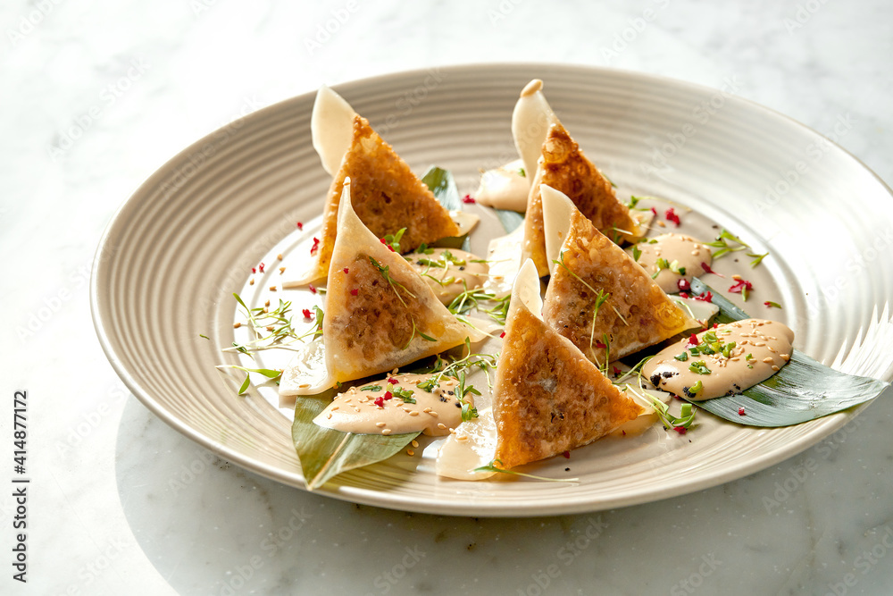 Fried dumplings or Japanese Gyoza in yellow sauce, cherry tomatoes and green peas, served in a white plate on a marble background. Pan-Asian cuisine. Restaurant food Fried dumplings or Japanese Gyoza in yellow sauce, cherry tomatoes and green peas, served in a white plate on a marble background. Pan-Asian cuisine. Restaurant food