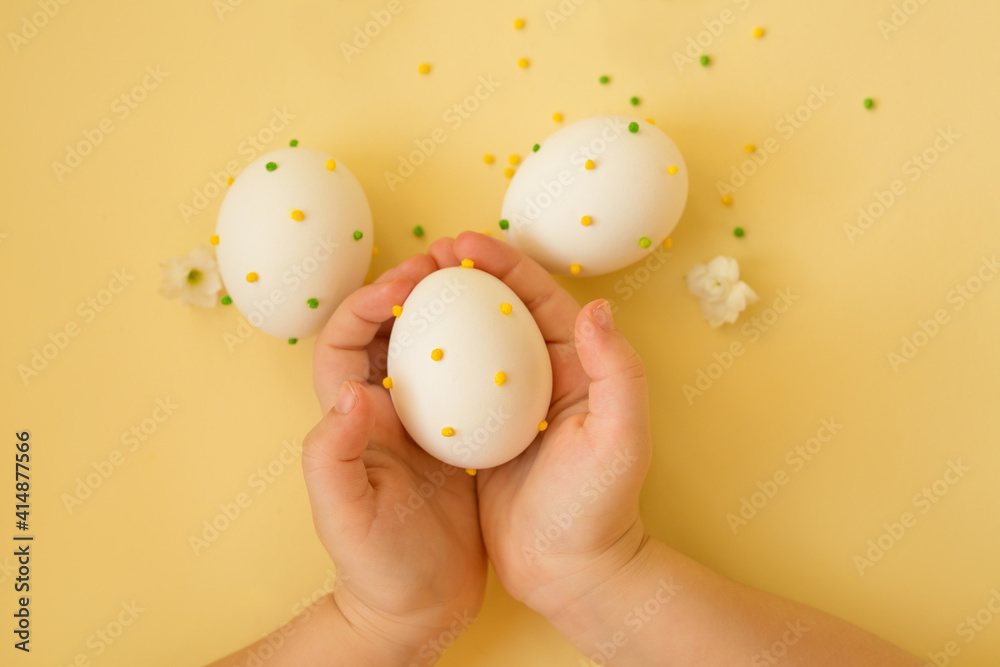 Easter eggs in the hands of a child.  The religious holiday of Easter. The decor of Easter eggs. Eggs with polka dots on a yellow background. 