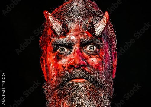 Halloween  blood on face. Devil horror concept. Demon with bloody horns on head. Man evil on black background close up.