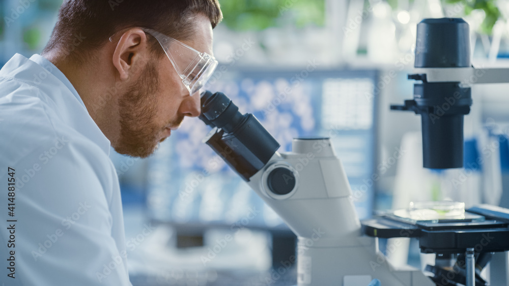 Shot of a Handsome Male Scientist Looking into the Microscope. Medical Scientist Working in a Modern Food Science Laboratory with Advanced Technology Microscopes and Computers. Shot of a Handsome Male Scientist Looking into the Microscope. Medical Scientist Working in a Modern Food Science Laboratory with Advanced Technology Microscopes and Computers.