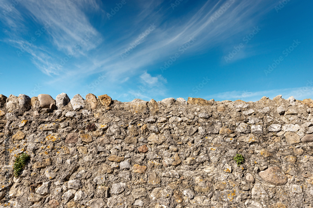 Closeup of a boundary wall made of stones and concrete in the countryside with blue sky and clouds on background. Verona province, Veneto, Italy, Europe.