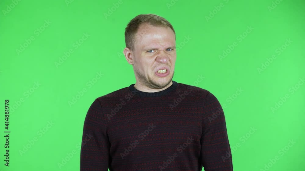Portrait of a middle aged men looking at the camera with disgust. Unshaven male in a black red sweater posing on a green screen in the studio. Close up. Portrait of a middle aged men looking at the camera with disgust. Unshaven male in a black red sweater posing on a green screen in the studio. Close up.